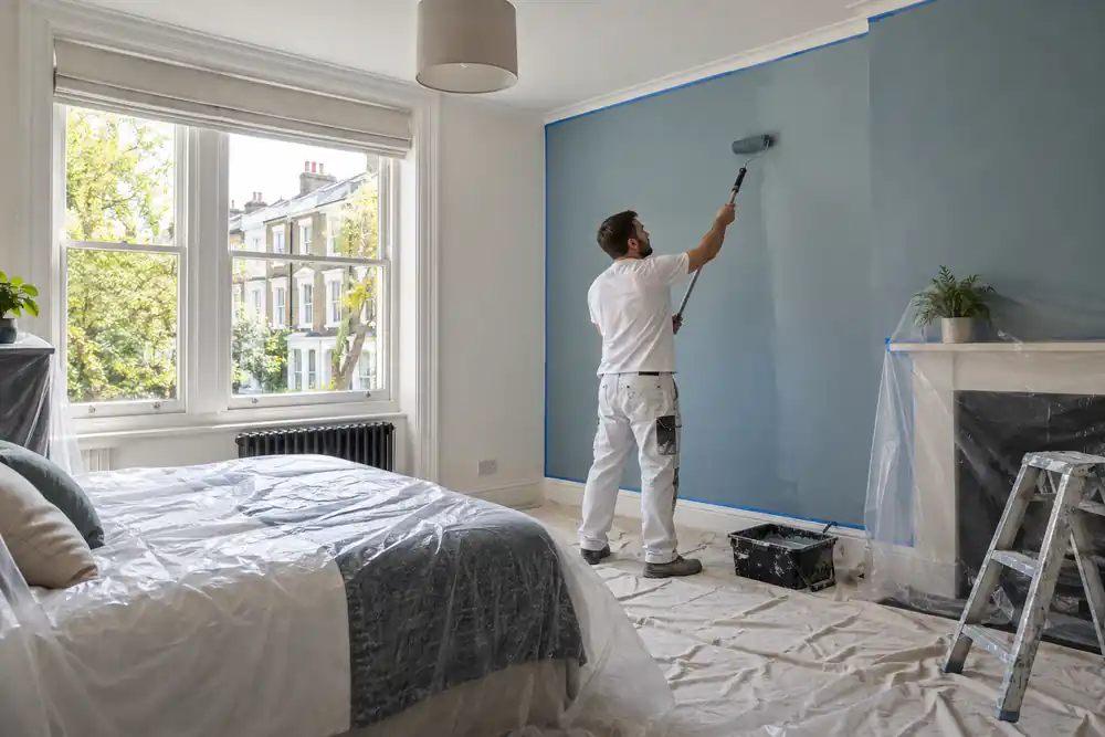 Decorator applying a new colour to a prepared bedroom wall