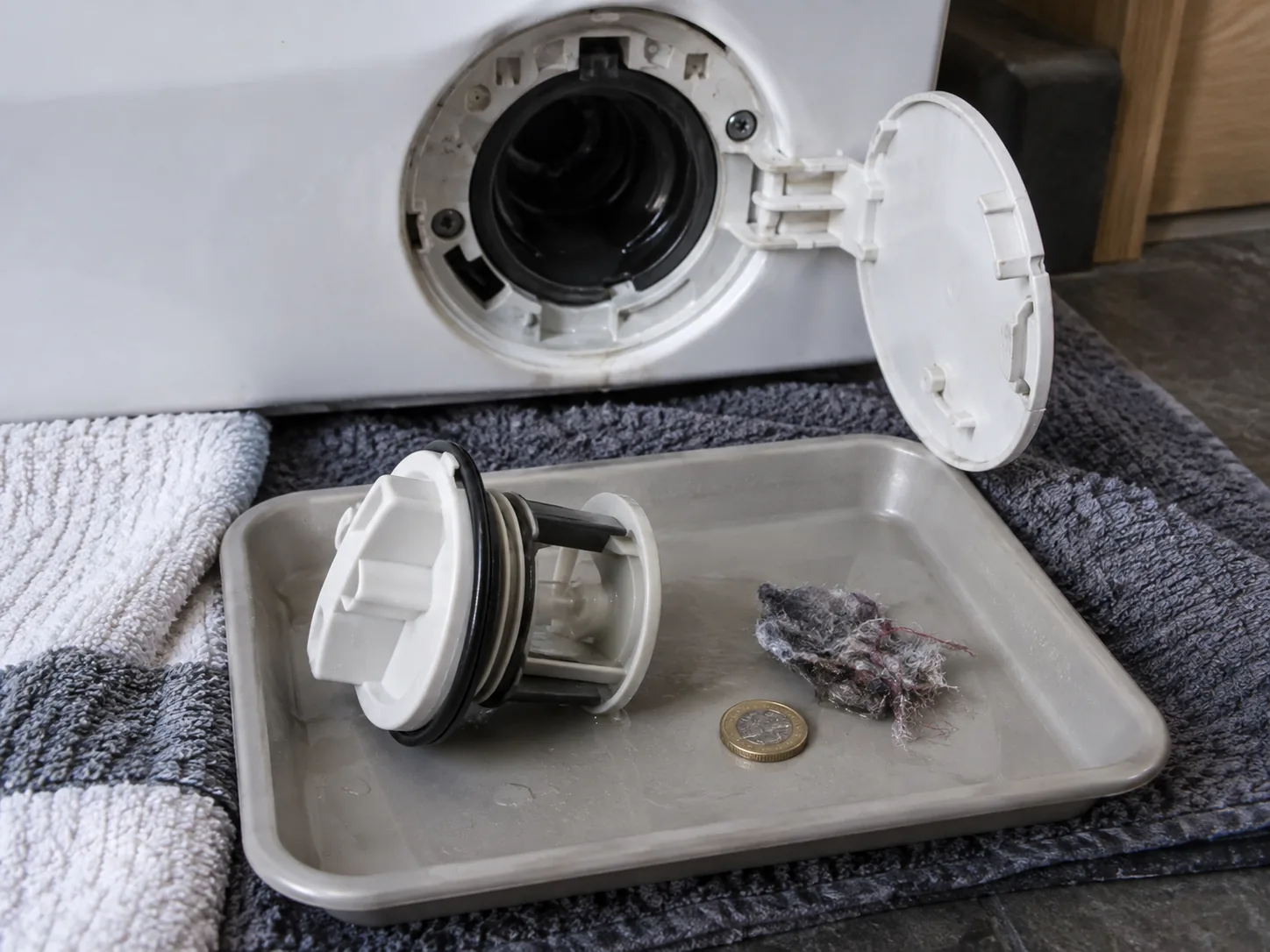 Removed washing-machine pump filter with lint and a coin in a shallow tray