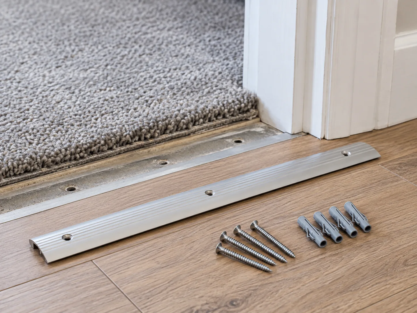 Removed aluminium threshold strip with screws and plugs beside a floor transition