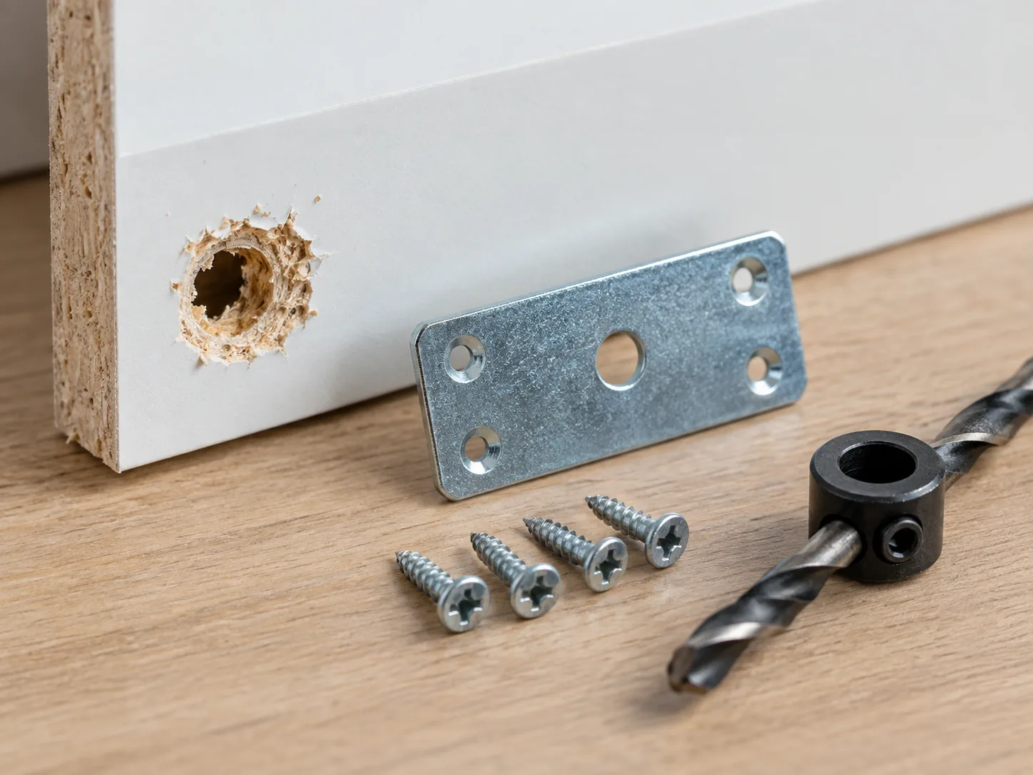 Stripped chipboard screw hole with a repair plate, short screws and drill stop collar