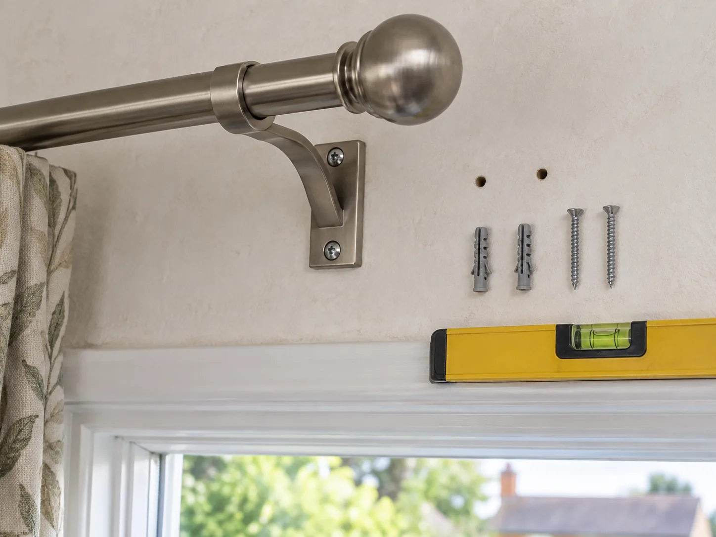 Secure curtain-pole bracket beside pilot holes, fixings and a spirit level